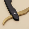 A close-up of a black and gold professional stainless steel shaver and beard razor kit.
