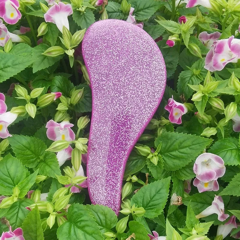 A close-up of a purple detangling hair brush surrounded by green foliage.