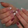 Une main présente un ensemble de faux ongles à presser roses français avec des accents floraux et un nail bordeaux profond.