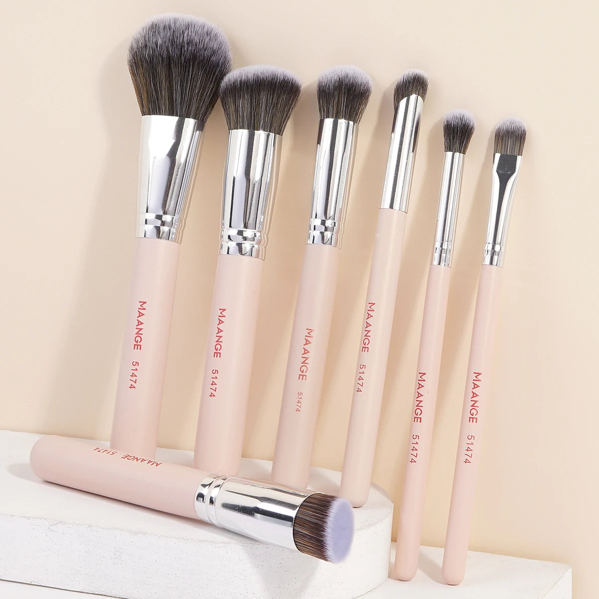 A set of seven professional makeup brushes with light pink handles and silver ferrules displayed against a neutral background
