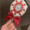 A hand holds a decorative makeup mirror set featuring red strawberries and gold accents on a white background.