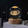 A glass crystal ball containing a galaxy night light rests on a wooden base.