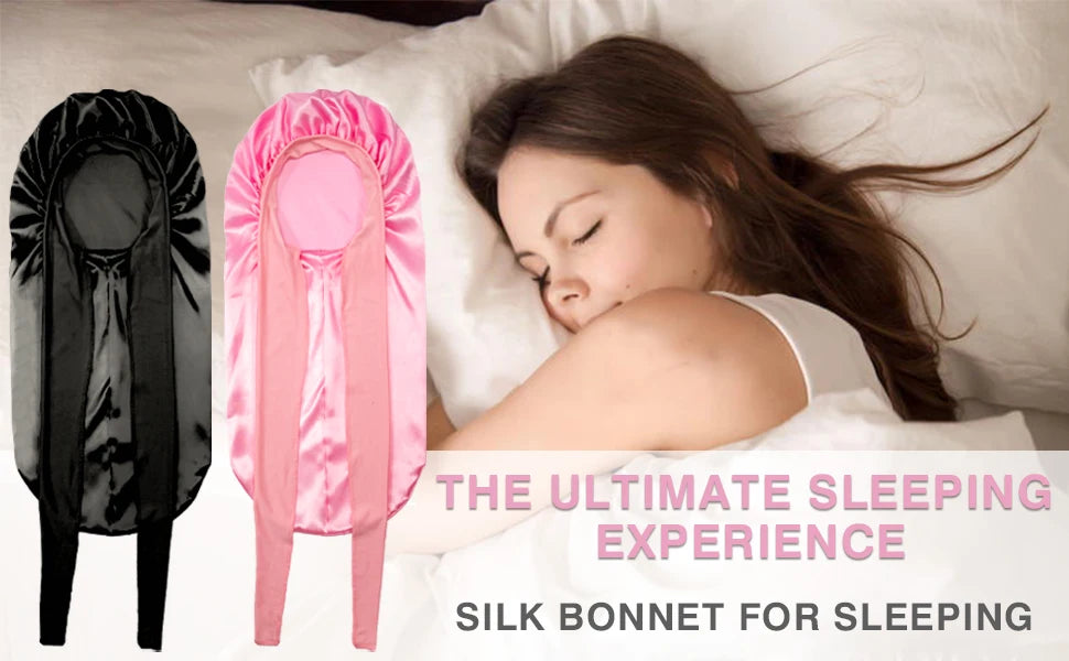 A woman is sleeping with a pink satin silk hair bonnet on her head, next to a black version.