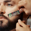 A hand is using a professional beard styling brush to groom a man's beard.