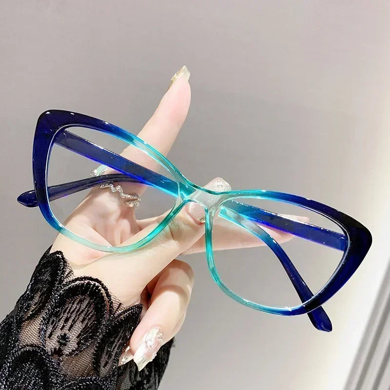 A hand holds a pair of blue-tinted cat eye reading glasses against a light gray background.