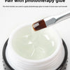 Gros plan d'un pinceau à ongles professionnel appliquant de la colle photothérapie sur une substance blanche dans un pot.