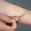 A hand is applying a disposable castor oil adhesive belly button patch onto the skin.