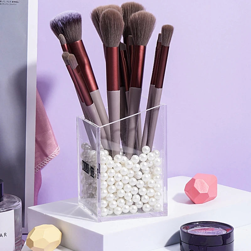 A collection of thirteen professional makeup brushes with various shades of brown and gray bristles displayed in a clear box.