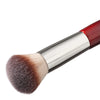 Primer plano de una brocha de maquillaje sintética roja y plateada multiusos con una punta densa y redondeada.