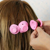 A hand is holding a set of pink heatless silicone curling hair tools against a person's brown hair.