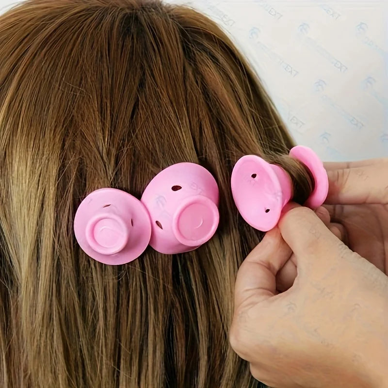 A hand is holding a set of pink heatless silicone curling hair tools against a person's brown hair.