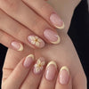 Gros plan d'une main présentant des kits de vernis press-on en forme de fleur à amande avec un dégradé rose pâle et crème.