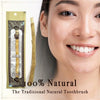 Close-up of a woman smiling, holding a traditional wooden miswak toothbrush packaged in a paper sleeve.