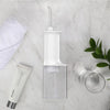 A clear portable dental water flosser device with a narrow nozzle and a glass jar is displayed on a marble surface.