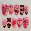 A set of ten press-on nails featuring a gradient pink and red design with various floral and fruit accents.