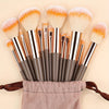 A collection of makeup brushes with soft synthetic bristles in various shades of orange and brown, resting on a pink cloth.