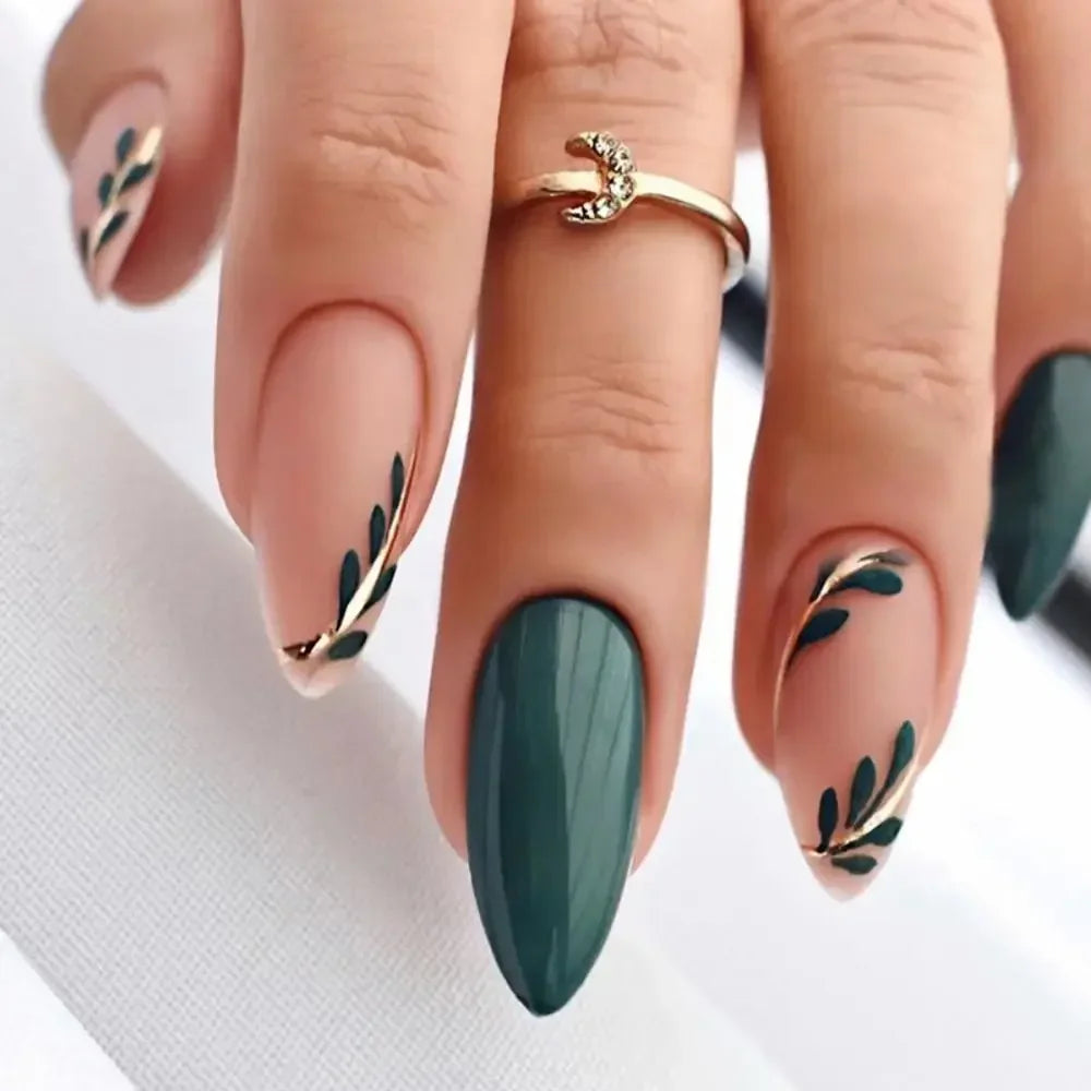 A hand displaying press-on false nails with a French wavy design featuring gold leaf accents on a dark green base.