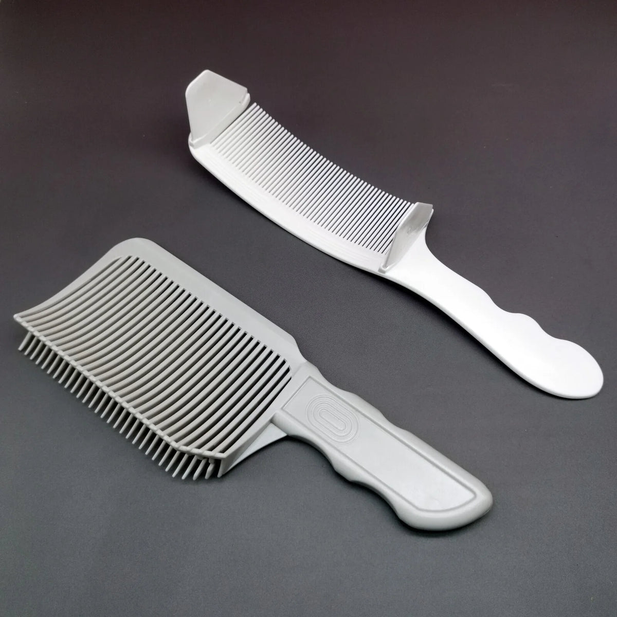 A set of professional flat top hair cutting combs, including a wide comb and a narrower comb, displayed on a dark surface.