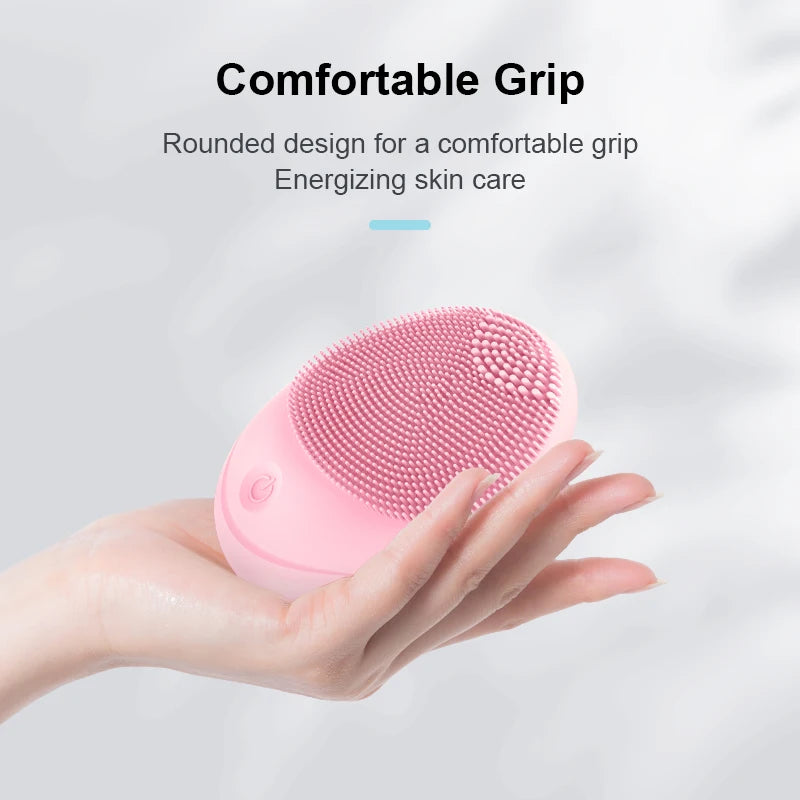A hand holds a pink electric sonic facial cleansing brush with a rounded design for skin care.