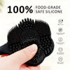 A hand holds a black silicone body brush with a dual-sided head, emphasizing its food-grade safety and suitability for travel
