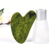 A green jade gua sha tool resting next to its silver container.