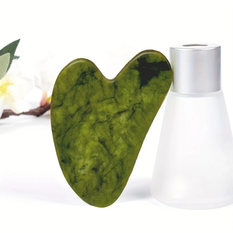 A green jade gua sha tool resting next to its silver container.