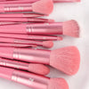 A collection of pink makeup brushes with gold accents laid out on a white surface.