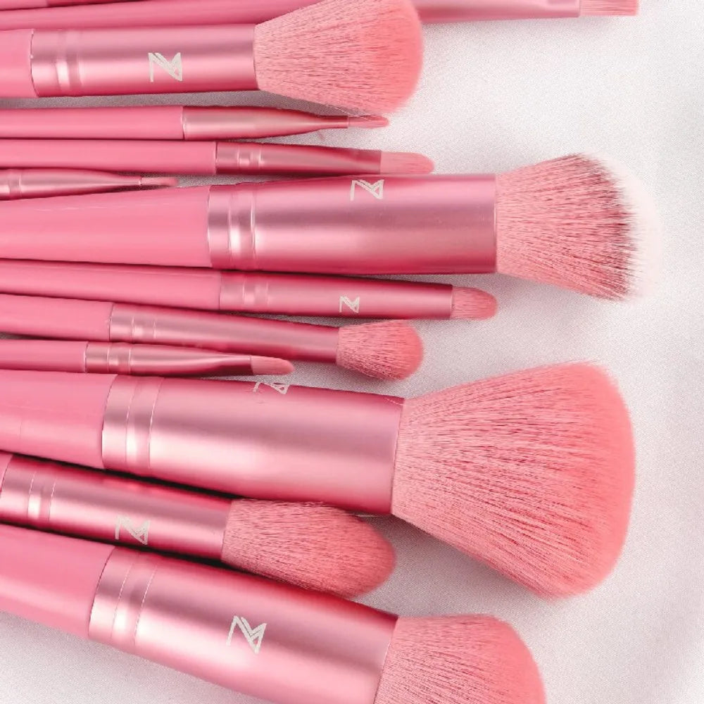 A collection of pink makeup brushes with gold accents laid out on a white surface.
