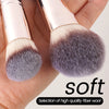 A close-up of a makeup brush showing soft gray and brown bristles on a wooden handle.