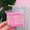 Une main tient un emballage plastique transparent de cotons-tiges en bambou rose pour un nettoyage doux.
