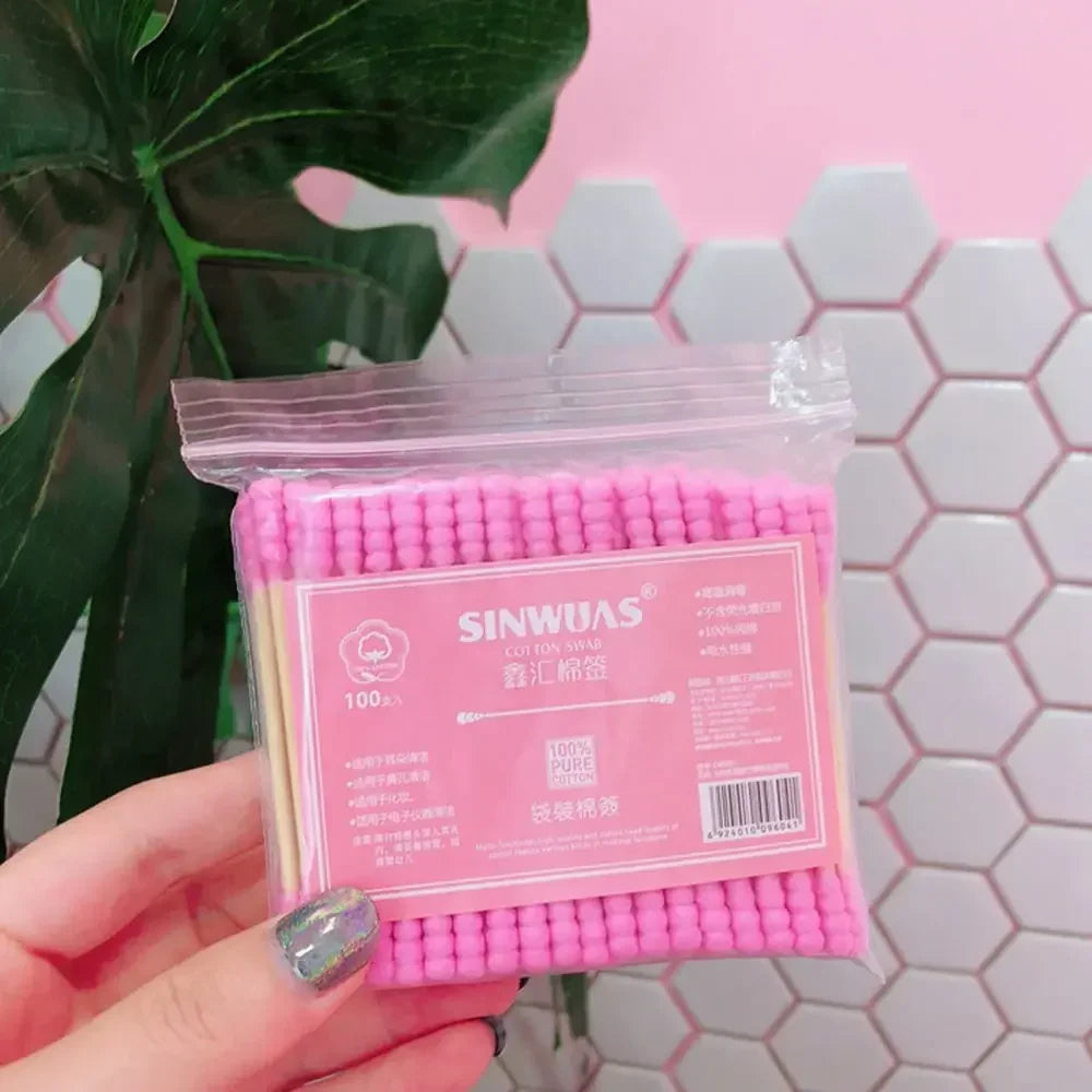 Une main tient un emballage plastique transparent de cotons-tiges en bambou rose pour un nettoyage doux.