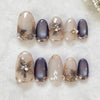 A set of 24 almond press-on nails featuring a glossy gray finish with gold floral and butterfly designs.