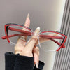 A hand holds a pair of red and clear cat eye reading glasses against a light gray background.