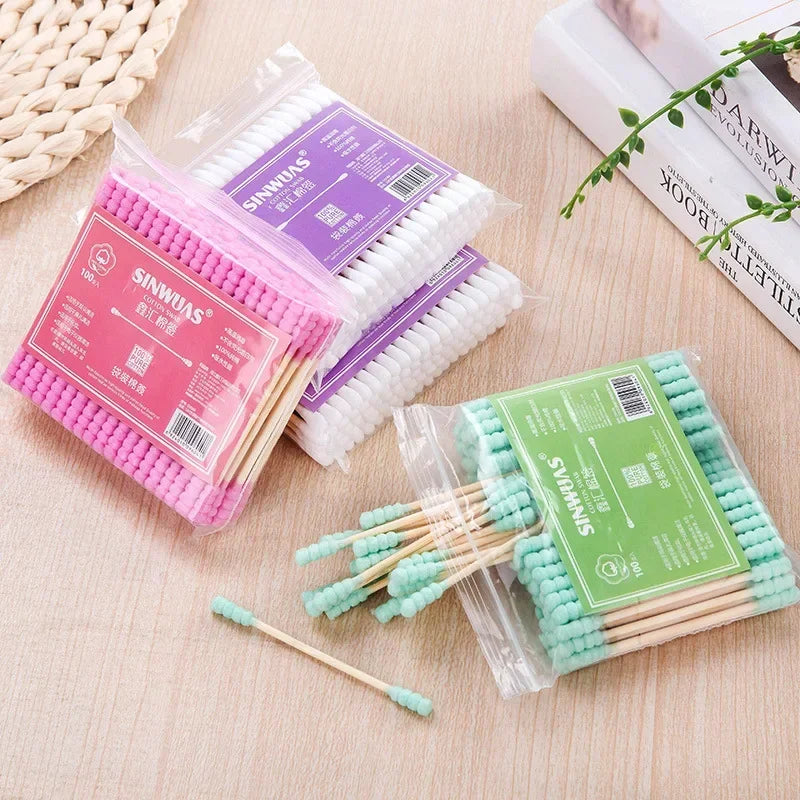 Une collection de cotons-tiges en bambou rose, violet et vert pour un nettoyage doux sont exposés sur une surface claire.