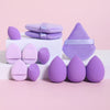 A collection of 12 purple and pink makeup sponges arranged on a white surface.