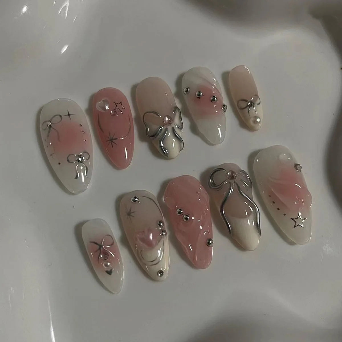 A collection of 24 pink heart pearl press-on fake nails displayed on a white surface.