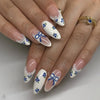 A hand displaying a set of pink heart pearl press-on fake nails with white and blue floral accents.