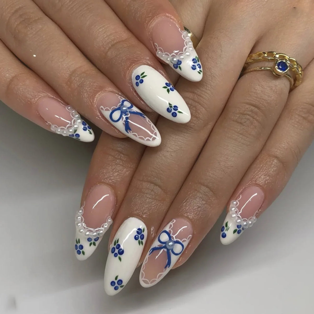 A hand displaying a set of pink heart pearl press-on fake nails with white and blue floral accents.
