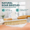 A wooden body exfoliating brush with natural boar bristles is shown on a person's skin.