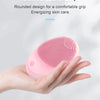 A hand holds a pink electric sonic facial cleansing brush with a rounded design.