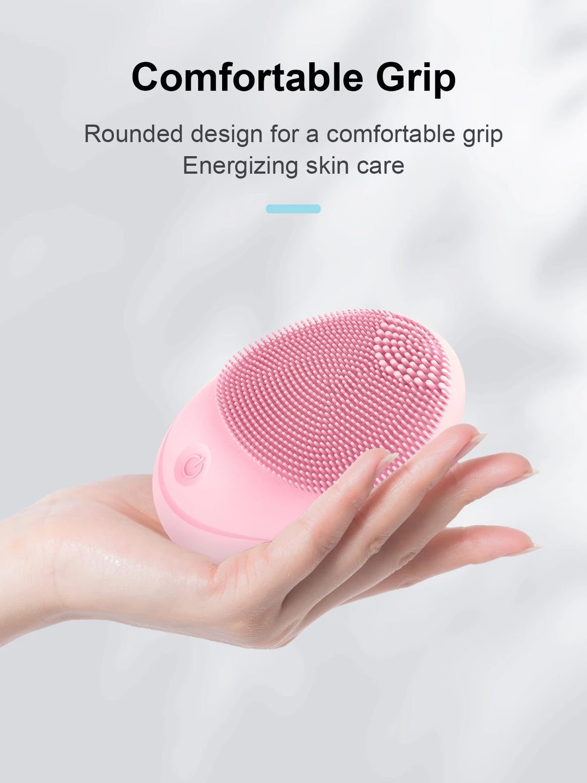 A hand holds a pink electric sonic facial cleansing brush with a rounded design.