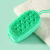 A bright green silicone body brush with bristles is resting on a white exfoliating towel.