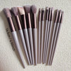 A collection of fifteen makeup brushes in various shades of pink and nude are displayed on a light background.