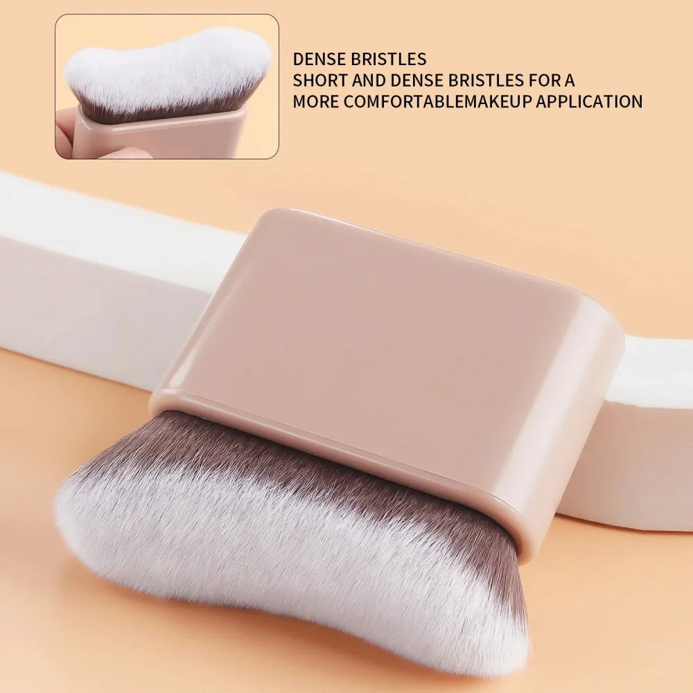 A close-up of a pink contour foundation brush with short, dense, angled wavy bristles resting on a light background.