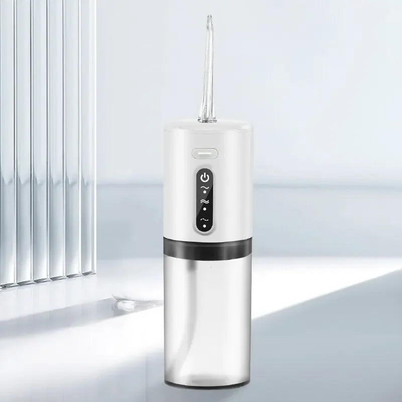 A silver portable electric water flosser with a clear tube and a black base sits on a light surface.