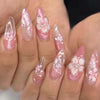 Close-up of a hand displaying pink cat eye false nails decorated with 3D floral and butterfly designs.