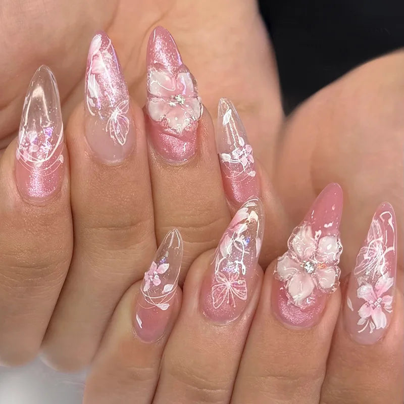 Close-up of a hand displaying pink cat eye false nails decorated with 3D floral and butterfly designs.