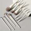 A set of fourteen professional makeup brushes with light wood handles and soft gray bristles arranged on a white background.