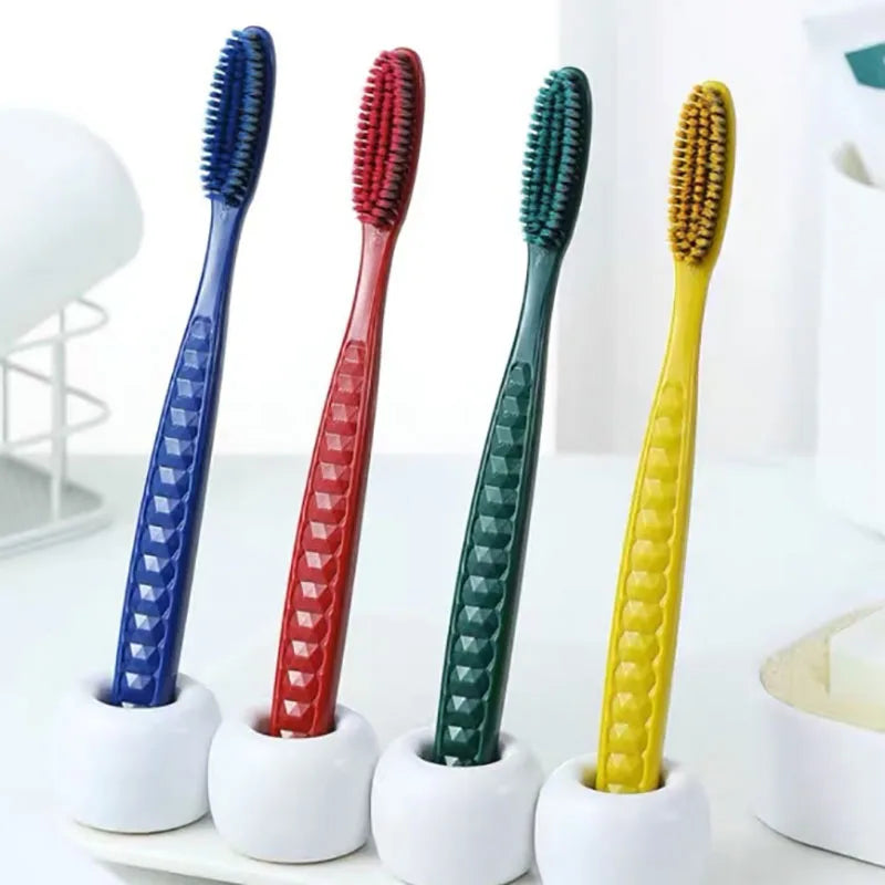 Un set de cinq brosses à dents colorées et douces, bleues, rouges, vertes et jaunes, sur une surface blanche.