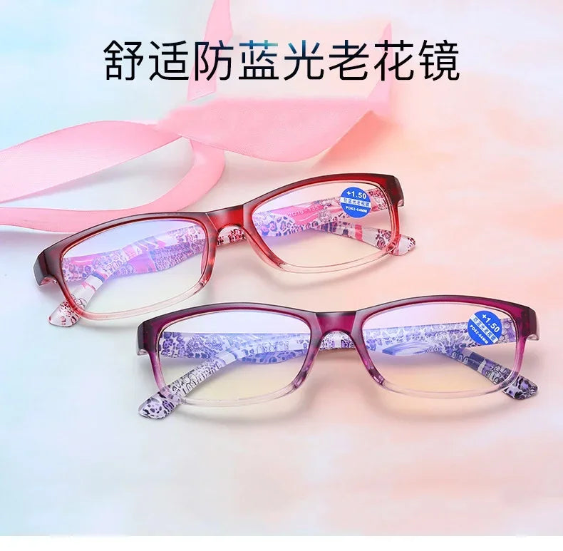 Pair of pink-framed reading glasses with purple patterned lenses shown against a light background.